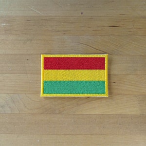 May include: A yellow, red, and green embroidered patch with a yellow border. The patch is the flag of Bolivia.