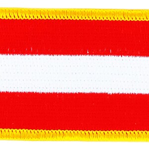 Könnte beinhalten: Ein gestickter Aufnäher mit der österreichischen Flagge. Der Aufnäher ist rot mit einem weißen Streifen in der Mitte und einem gelben Rand.