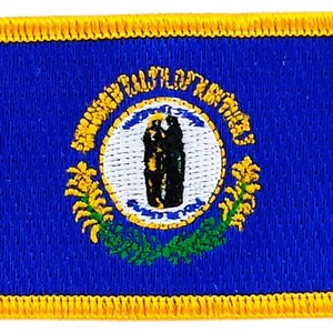 May include: A blue embroidered patch with a yellow border. The patch features the state seal of Virginia, which includes a depiction of a woman holding a liberty cap and a spear, surrounded by a wreath of flowers.