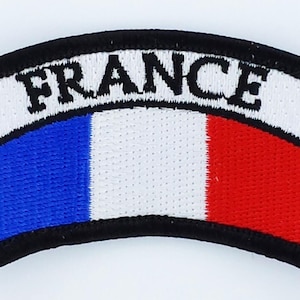 Op de afbeelding: Geborduurde patch met het woord "FRANCE" in zwart op een witte achtergrond. Daaronder wordt de Franse vlag afgebeeld met blauwe, witte en rode strepen. De patch heeft een zwarte rand.
