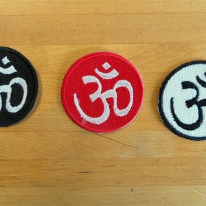 May include: Three round embroidered patches with the Om symbol. The patches are black, red, and white with white, red, and black Om symbols respectively.