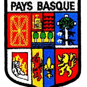 Peut inclure: Écusson brodé avec l'inscription "PAYS BASQUE" au-dessus d'un blason. Le blason est divisé en six sections, chacune avec des symboles différents en rouge, jaune, bleu et blanc. Il a une bordure noire.