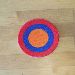 May include: A red, blue, and orange embroidered circle patch. The patch has a concentric circle design with a red outer ring, a blue middle ring, and an orange inner circle.