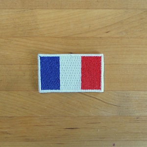 Könnte beinhalten: Ein kleiner gestickter Aufnäher der französischen Flagge. Die Flagge ist blau, weiß und rot.
