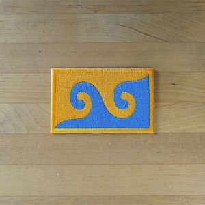 May include: A blue and yellow embroidered patch with a stylised wave design.