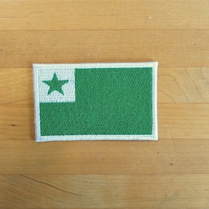 Op de afbeelding: Een groene en witte geborduurde patch met een witte ster in de linkerbovenhoek. De patch is rechthoekig en heeft een witte rand.