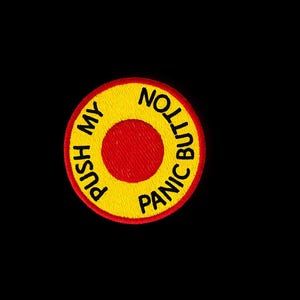 Op de afbeelding: Geborduurde patch met een gele buitenring en een rode kern. De tekst "PUSH MY BUTTON PANIC BUTTON" is in zwart rond de cirkel geborduurd. De patch is geplaatst tegen een zwarte achtergrond.