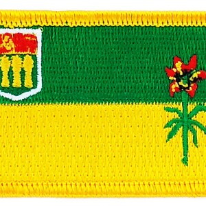May include: An embroidered patch in yellow and green, featuring the coat of arms of the province of Alberta, Canada. The coat of arms is a shield with a red lion on a white background. The shield is surrounded by a white border and is topped with a crown. The patch also features a green and red flower with a green stem.
