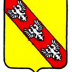 May include: A heraldic shield with a yellow background and a red diagonal stripe. Three white eagles are arranged along the red stripe. The shield has a pointed base and a black border.