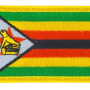 May include: An embroidered patch featuring the flag of Zimbabwe. The patch is yellow, red, black, and green with a white triangle containing a bird and a star. The patch has a yellow border.