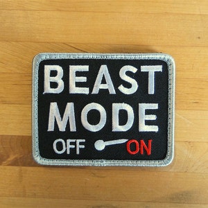 Può includere: Toppa nera con testo ricamato in bianco "BEAST MODE" e un interruttore a levetta bianco con le parole "OFF" e "ON" in rosso.