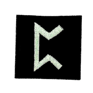 Op de afbeelding: Een zwart vierkant embleem met een lichtgroen geborduurd rune-symbool. De rune is een gestileerd, hoekig ontwerp, gecentreerd op het embleem. De borduursels hebben een getextureerd uiterlijk tegen de effen zwarte achtergrond.