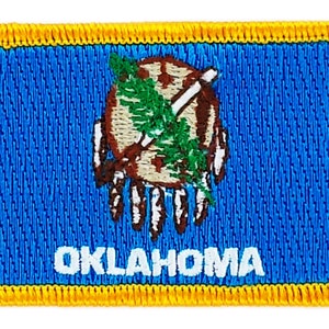 May include: An embroidered patch featuring the state flag of Oklahoma. The patch is blue with a yellow border and depicts the state seal, which includes a Native American hand holding a peace pipe and a bundle of arrows. The text "OKLAHOMA" is written in white below the seal.