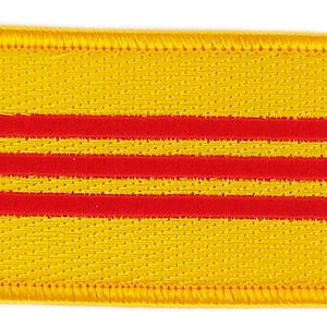 May include: A yellow fabric patch with three red horizontal stripes. The patch has a yellow border.