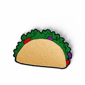 Könnte beinhalten: Gestickter Taco-Aufnäher mit einer beigen Tortilla, grünem Salat, roten Tomaten und lila Zwiebeln. Der Aufnäher hat einen schwarzen Rand und befindet sich auf weißem Hintergrund. Für Kleidung und Accessoires.