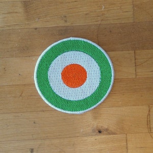 May include: An embroidered patch with a bullseye design in green, white and orange.