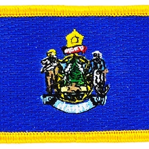 May include: A blue embroidered patch with a yellow border. The patch features the state seal of Maine, which includes a pine tree, a moose, and a farmer.