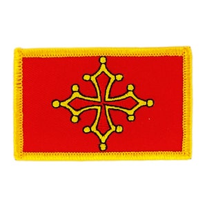 May include: A red embroidered patch featuring a yellow cross with a distinctive design, surrounded by small circles. The patch has a yellow border.