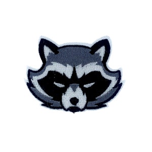 Puede incluir: Un parche bordado de la cara de un mapache, en negro y gris.