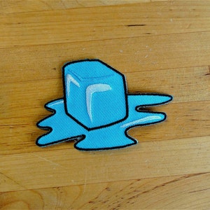 Peut inclure: Un glaçon bleu fondant sur une flaque bleue. Le glaçon est bordé de noir et a un intérieur blanc. La flaque est bordée de noir.