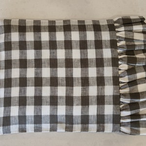 May include: A brown and white gingham pillow with a ruffled edge. The pillow is made of a soft, linen fabric.