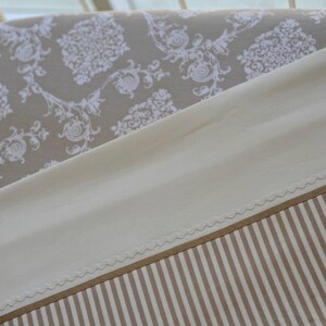 May include: A beige and white patterned fabric with a white scalloped edge. The fabric is folded over a white and beige striped fabric.