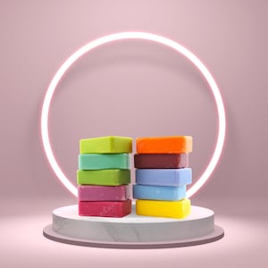 May include: A stack of colorful soap bars on a white marble pedestal with a neon pink circle in the background.