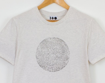May include: A beige t-shirt with a black circle design printed on the front. The circle is filled with a pattern of small black lines. The shirt has a crew neck and short sleeves. The brand name "I-O" is printed on the tag.