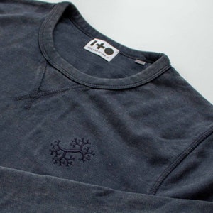 May include: A dark blue long-sleeved shirt with a small embroidered design on the left chest. The shirt has a crew neck and a label that reads "1+0 ONE AND OTHER O".