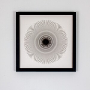May include: A black framed print with a white background and a black and white geometric design of concentric circles radiating outward from the center.