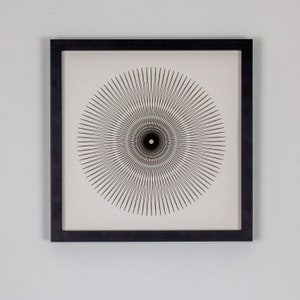 May include: A black and white framed print of a geometric design with a circular pattern of radiating lines.