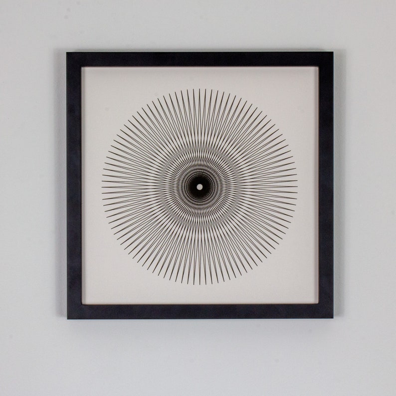 May include: A black and white framed print of a geometric design with a circular pattern of radiating lines.