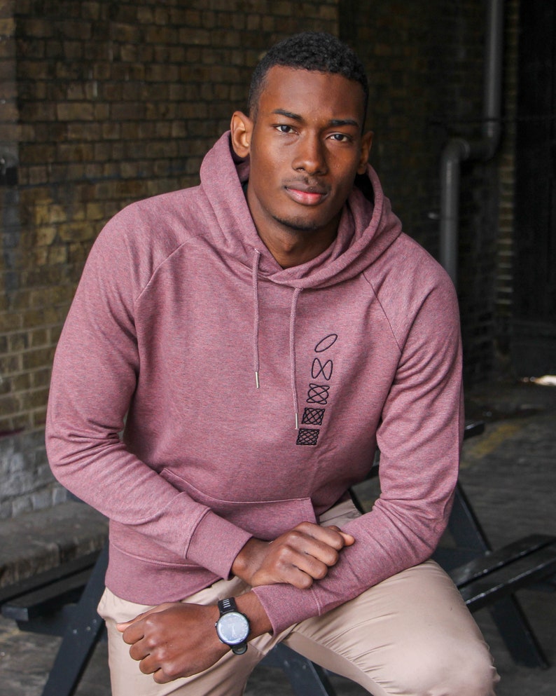 Op de afbeelding: Een maroon hoodie met een zwart geometrisch ontwerp op de voorkant. De hoodie heeft een capuchon met trekkoord en een kangoeroezak.