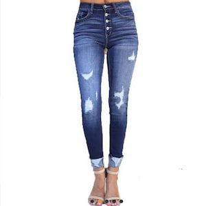 Könnte beinhalten: Dunkelblaue Jeans mit hoher Taille und Knopfleiste. Die Skinny-Jeans hat Distressed-Details mit zerrissenen Stellen an den Beinen. Die Manschetten sind hochgekrempelt.