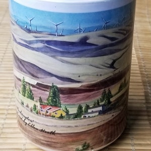 May include: White ceramic mug with a colorful landscape scene featuring wind turbines, rolling hills, and a small town. The mug has the text "Washington" and "by Ellen Heath" printed on the bottom.