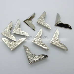 Peut inclure: Dix protège-coins argentés avec un motif orné. Les protège-coins sont en forme de triangle rectangle.