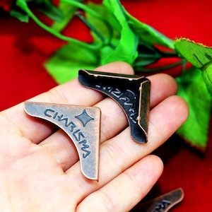 Puede incluir: Dos protectores de esquina de cobre antiguo con la palabra "CHARISMA" grabada en uno y un diseño decorativo en el otro.