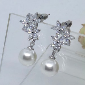 May include: A pair of silver earrings with a pearl drop and a cluster of clear cubic zirconia stones in the shape of flowers.