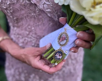 Puede incluir: Un ramo de novia blanco con dos dijes de fotos dorados. Los dijes muestran fotos de una pareja mayor y una pareja más joven. El ramo lo sostiene una persona que lleva un vestido morado claro.