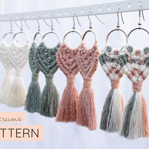 May include: Four pairs of macrame earrings with tassels in various colours, including white, green, pink, and a combination of white, green, and pink. The earrings are hanging from a white rack.