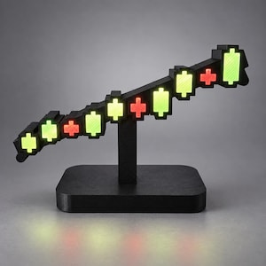 May include: A black desktop display featuring a series of illuminated pixelated candlestick chart blocks. The blocks are arranged in an upward trend, alternating between glowing green and red colors, supported by a central black rectangular base.