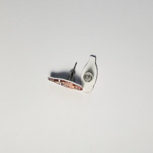 K&ouml;nnte beinhalten: Ein Paar Ohrstecker mit einem braunen und wei&szlig;en Design. Die Ohrringe sind aus Metall und haben einen Stiftverschluss.