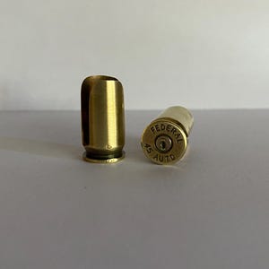 May include: Two gold-colored bullet casings. One casing is standing upright and the other is lying on its side. The casing on its side has the text "FEDERAL 45 AUTO" engraved on it.