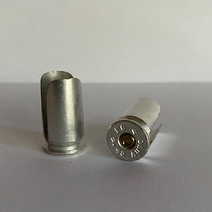 May include: Two silver-colored bullet casings, one with the inscription "45 AUTO FC" visible. The casings are used as decorative items.