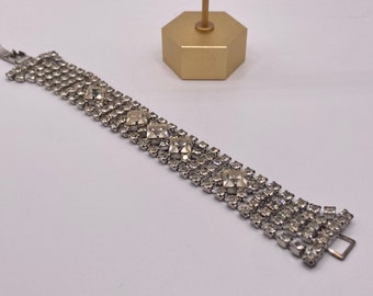 May include: A silver bracelet with a row of clear square rhinestones. The bracelet has a clasp closure.