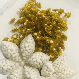 May include: A bouquet of white and gold flowers. The white flowers are made of small, round beads and are arranged in a star shape. The gold flowers are made of thin, delicate petals and are arranged in a cluster.