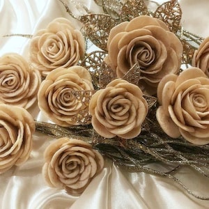 May include: A bouquet of cream-colored, paper roses with a gold glitter background. The roses are arranged in a circular pattern and have a delicate, layered appearance.
