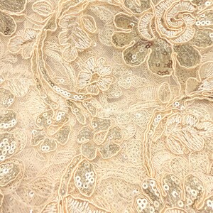 May include: A light beige lace fabric featuring intricate floral embroidery with matching thread and shimmering silver sequins. The design consists of swirling vines, leaves, and blossoms layered over a delicate, fine-mesh netting base.