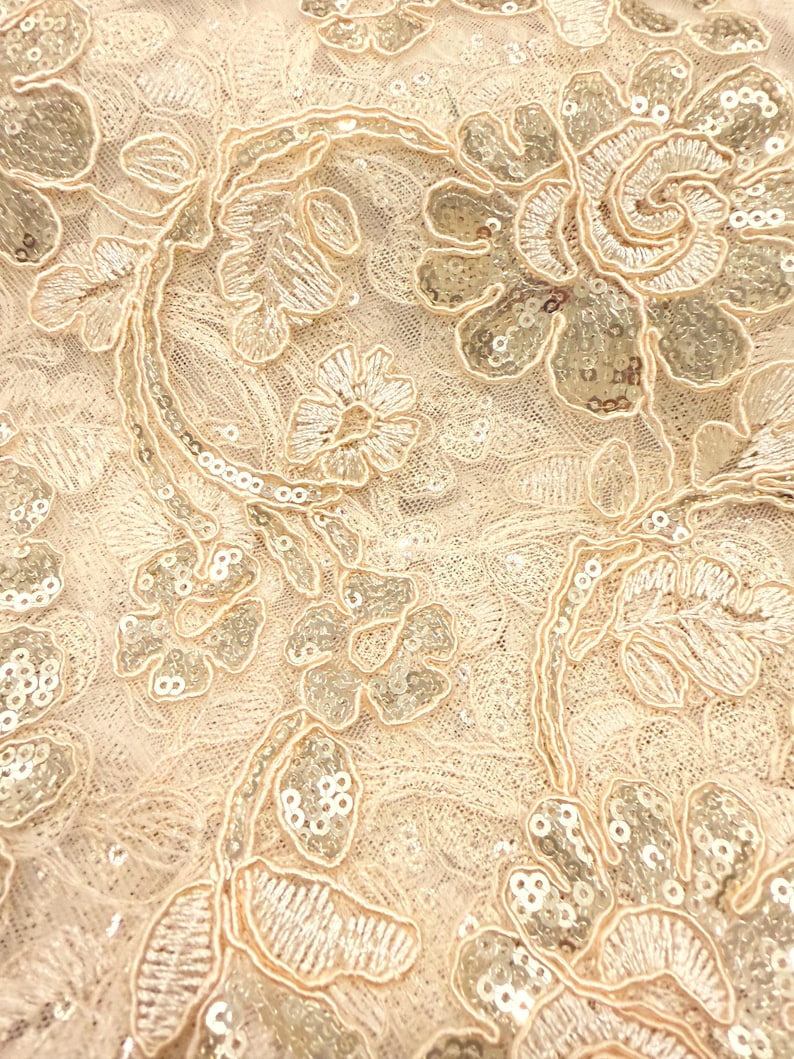 May include: A light beige lace fabric featuring intricate floral embroidery with matching thread and shimmering silver sequins. The design consists of swirling vines, leaves, and blossoms layered over a delicate, fine-mesh netting base.