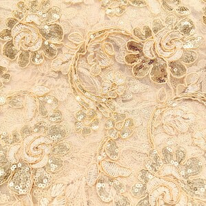 May include: A light beige lace fabric featuring an intricate floral pattern embroidered with matching thread and embellished with small, shimmering gold sequins throughout the petals and leaves, creating a textured and reflective surface design.